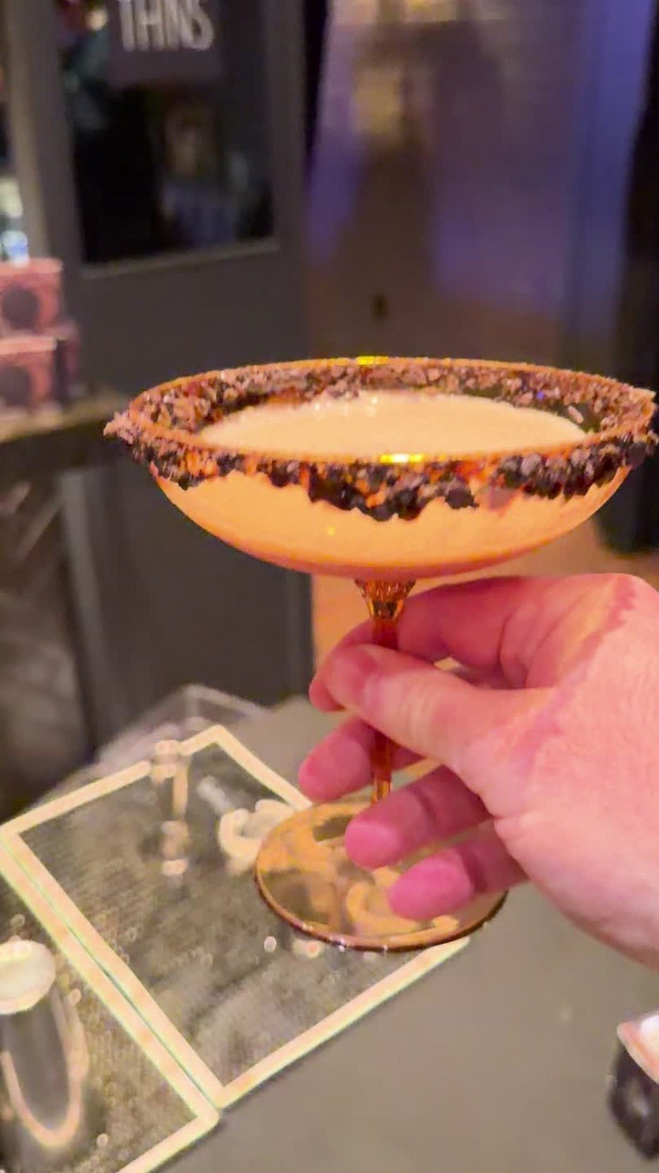 A coupe glass with a cookie-crumb rim at the launch. Video still.